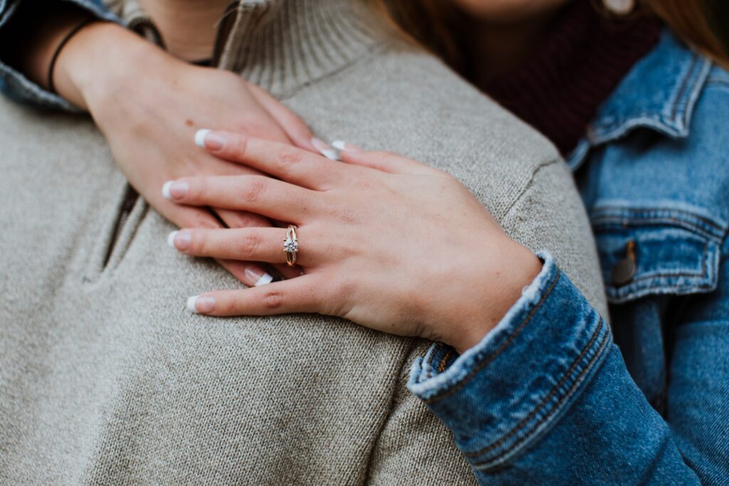 girl holding her hands over her fiancé's chest, showing her engagement ring