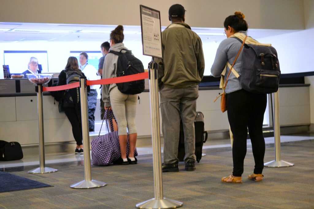 People standing in line at the ticket counter of a busy airport with their luggage and suitcases